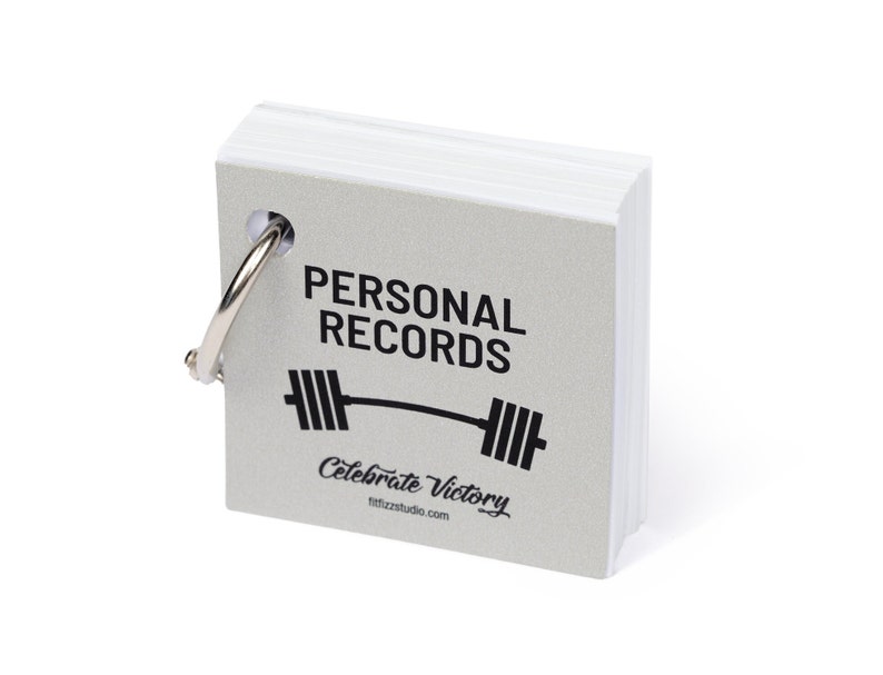 Close-up of the front of the notepad. The cover is silver paper that says Personal Records with a barbell underneath. Bound with a silver ring.