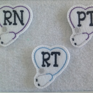 May include: Three felt heart-shaped patches with a stethoscope design and the letters RN, PT, and RT in black embroidery.