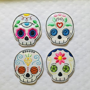 May include: Four white sugar skull patches with colorful embroidery. Each skull has a different design with flowers, swirls, and eyes.
