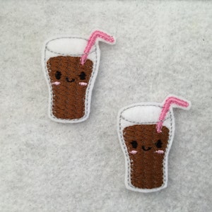 May include: Two brown and white felt appliques of a cartoon soda glass with a pink straw and a smiling face.
