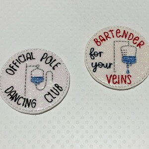 May include: Two round, glittery patches. One reads "OFFICIAL POLE DANCING CLUB" with a blue IV bag graphic. The other says "BARTENDER for your VEINS" with a similar IV bag graphic in blue.