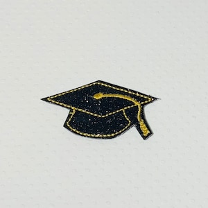 May include: Black graduation cap with a gold outline and tassel. The cap is made of felt and has a sparkly finish.