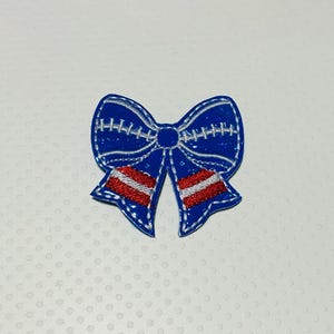 May include: Blue and red embroidered bow with white stitching. The bow is a patriotic design with red and white stripes.
