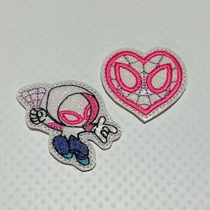 May include: Two embroidered patches featuring a superhero theme. One patch depicts a character in a white and pink costume, while the other is a heart-shaped design with a spiderweb pattern. Both patches have a glittery finish.