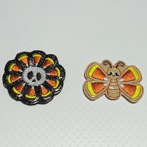 May include: Two iron-on patches, one with a skull surrounded by candy corn and the other with a butterfly with candy corn wings.