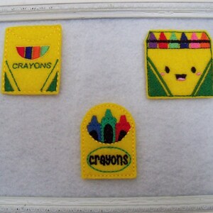 May include: Three felt patches with a crayon theme. The first patch is a yellow box with the word "CRAYONS" on it. The second patch is a yellow box with a smiling face and the words "CRAYONS" on it. The third patch is a yellow box with a row of crayons inside.