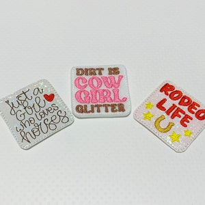 May include: Three white iron-on patches with pink, red, and brown embroidery. The patches read "Just a girl who loves horses", "Dirt is Cow Girl Glitter", and "Rodeo Life U".