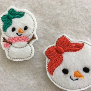 May include: Two felt snowman ornaments, one with a green bow and pink scarf, the other with a red bow.