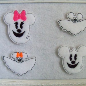 May include: Four white felt ghost ornaments with black eyes and mouths. Two ghosts have black bat wings and one has a pink bow. The ghosts are displayed on a white background.