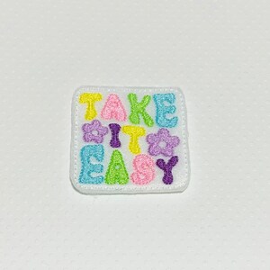 May include: A white embroidered patch with the phrase "Take it easy" in colorful letters and flowers.
