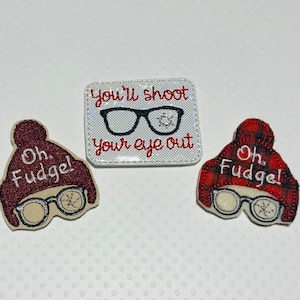 May include: Three felt patches with a Christmas theme. One patch is red and white plaid with the text "Oh. Fudge!" and a pair of glasses with a snowflake. Another patch is maroon with the text "Oh. Fudge!" and a pair of glasses with a snowflake. The third patch is white with the text "You'll shoot your eye out" and a pair of glasses with a snowflake.