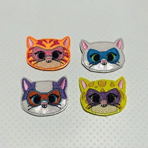 May include: Four embroidered iron-on patches featuring cartoon cats wearing superhero masks. The cats are orange, white, purple, and yellow.