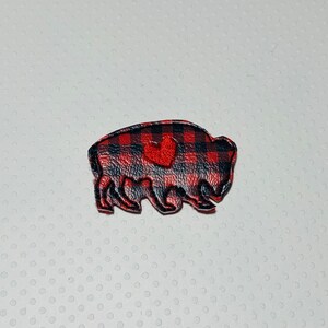 May include: Red and black buffalo plaid fabric applique with a red heart in the center. The applique is shaped like a buffalo.