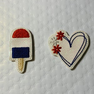 May include: Two embroidered patches, one a red, white, and blue popsicle and the other a white heart with red flowers and blue stitching.