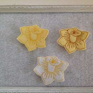 May include: Three felt flower appliques, two yellow and one white, with gold embroidery, displayed on a white background.