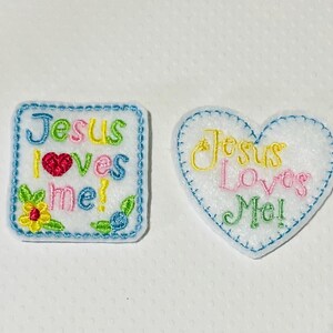 May include: Two embroidered iron-on patches with the text "Jesus Loves Me!" in different colors. One patch is a square with a blue border and the other is a heart shape with a blue border.