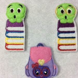 May include: Three felt appliques featuring a green monster with glasses and a stack of books, a green monster with a stack of books, and a purple backpack with a heart and glasses.