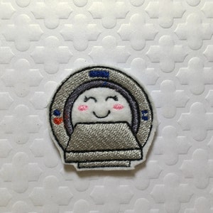 May include: Embroidered patch of a cartoon MRI machine with a smiling face. The machine is gray and white with blue accents.
