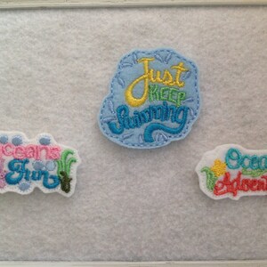 May include: Three embroidered patches with ocean-themed designs. The first patch is white with blue, pink, and green embroidery and says "Oceans of Fun". The second patch is light blue with yellow and blue embroidery and says "Just Keep Swimming". The third patch is white with yellow, green, and red embroidery and says "Ocean Adventures".