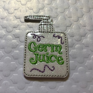 May include: White glitter hand sanitizer bottle with a green embroidered label that says "Germ Juice".