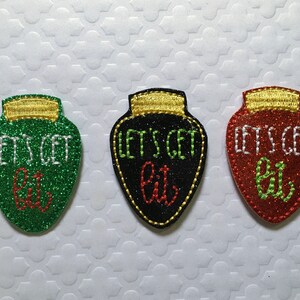 May include: Three Christmas light bulb ornaments with glitter. Each ornament is a different color: green, black, and red. The ornaments have white text that says "Let's Get Lit".