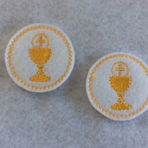 May include: Two white felt circles with gold embroidered chalices and crosses. The chalices have a round top with a cross and a round base.