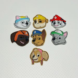 May include: Eight embroidered felt patches featuring the characters from the children's TV show Paw Patrol. The patches are in various colors and feature the characters' faces and hats.