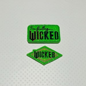 May include: Two green glitter iron-on patches with the text "I'm feeling wicked" and "Wicked" in black lettering.