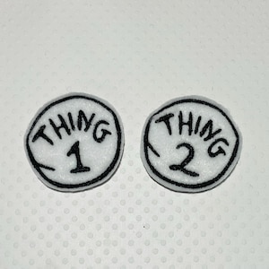 May include: Two white circular patches with black stitched borders. Each patch has the word "THING" arched above a number. One patch has the number "1" and the other has the number "2".