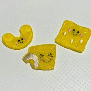 May include: Three yellow felt patches with embroidered faces. The patches are shaped like a macaroni noodle, a square, and a curved shape.
