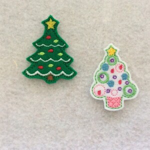May include: Two felt Christmas tree ornaments. One is green with yellow lights and red ornaments. The other is white with colorful circles and a pink base.