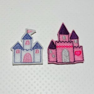 May include: Two embroidered castle patches. One is white with blue and pink accents, and the other is pink with purple accents. Both have a whimsical, fairytale design, perfect for embellishing clothing or accessories.