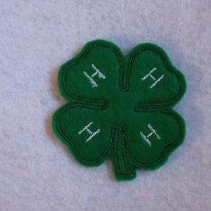 May include: A green four-leaf clover patch with white embroidered "H"s on each leaf.
