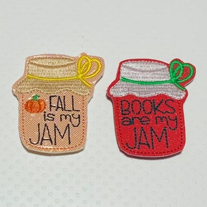 May include: Two embroidered iron-on patches shaped like jars of jam. One is peach colored with the text "Fall is my jam" and a small pumpkin. The other is red with the text "Books are my jam".