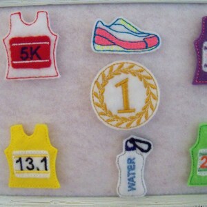 May include: A collection of felt patches featuring running-themed designs, including a gold medal with the number "1", a water bottle, and running vests with the numbers "5K", "10K", "13.1", and "26.2".