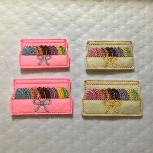 May include: Two sets of felt boxes with a stack of colorful felt circles inside. One set is pink and the other is beige.