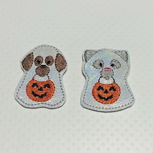May include: Two Halloween-themed patches. One patch is a dog with brown ears and spots, and the other is a cat. Both are holding orange jack-o'-lanterns. The patches have a silver, glittery appearance and are outlined with a dotted stitch.