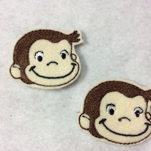May include: Two brown felt patches with embroidered faces of a cartoon monkey. The monkey has a brown face, white eyes, and a brown smile.