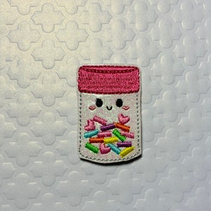 May include: A pink and white embroidered jar with a smiling face and filled with colorful sprinkles.