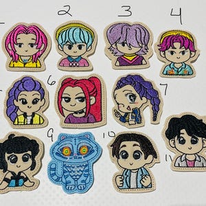 May include: A collection of eleven embroidered patches. The patches feature cartoon-style characters with various hairstyles and outfits. One patch depicts a blue raccoon. The patches are outlined in a tan color.