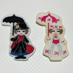 May include: Two fabric appliques featuring a woman holding an umbrella. One is dressed in a black coat, red scarf, and blue skirt, with a black hat. The other is in a white dress with red accents and a pink umbrella.