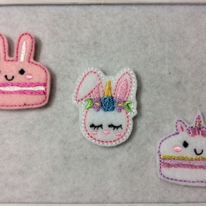 May include: Three felt appliques featuring a pink bunny cake, a white bunny with a unicorn horn and flowers, and a white unicorn cake. The appliques are perfect for adding a whimsical touch to crafts and projects.