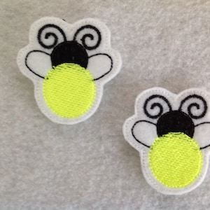 May include: Two white felt embroidered firefly patches with black antennae and wings. The fireflies have yellow bodies.