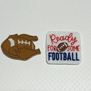 May include: Two embroidered iron-on patches. One patch is brown and shaped like a football. The other patch is white with red and blue embroidery and says "Ready for some Football".