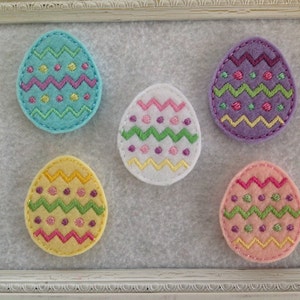 May include: Five felt Easter eggs with different embroidered designs. Each egg features a zig-zag pattern, dots, and a combination of pink, green, yellow, purple, and blue colors.