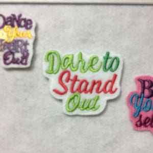 May include: Three embroidered iron-on patches with inspirational messages. The first patch is yellow, green, and purple and says "Dance Your Heart Out". The second patch is white with green and red lettering and says "Dare to Stand Out". The third patch is pink with purple, blue, and turquoise lettering and says "Be Yourself!"