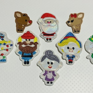 May include: Set of eight embroidered iron-on patches featuring Christmas characters. The patches include a snowman, a Christmas tree, Santa Claus, a reindeer, a girl with blonde hair, a man with a beard, and two reindeer.