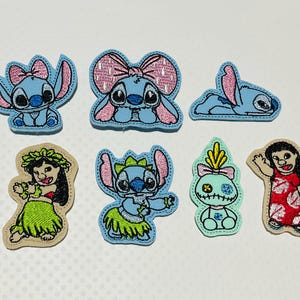 May include: A collection of embroidered patches featuring characters from a popular animated film. The patches include the blue alien character with pink accents, and a girl in a red dress and green skirt. The patches are on a white background.