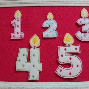 May include: Five felt birthday candles in the shape of numbers 1 through 5. The candles are white with colorful flames and polka dots. The candles are displayed on a red background.