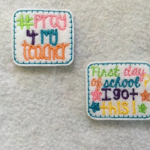 May include: Two felt patches with embroidered text. The first patch is light blue with a white border and says "#Pray 4 my teacher" in colorful thread. The second patch is white with a light blue border and says "First day of school? I got this!" in colorful thread with stars.
